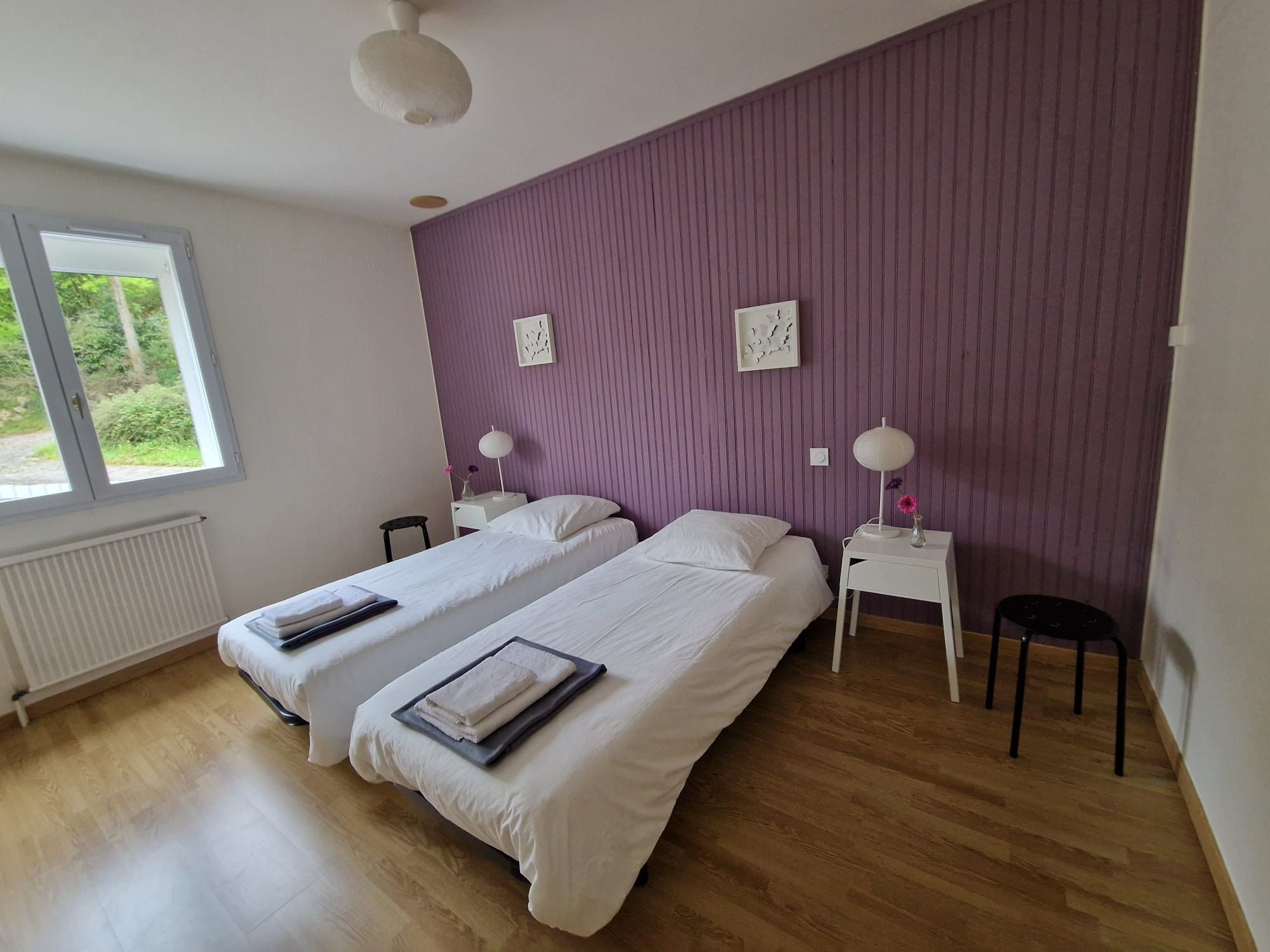 Une chambre avec deux lits, une fenêtre, un radiateur et un mur de couleur violette.