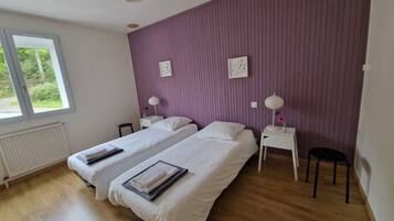 Une chambre avec deux lits, une fenêtre, un radiateur et un mur de couleur violette.
