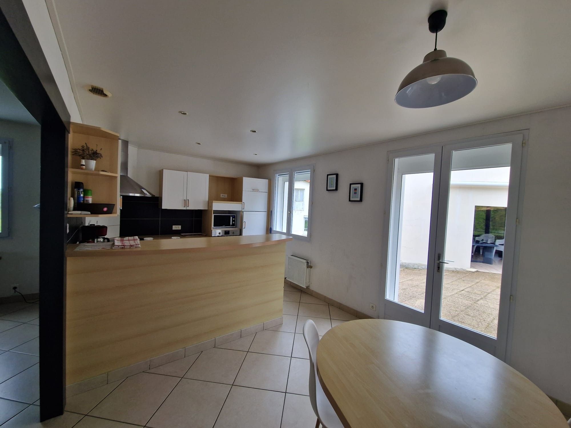 Cozinha moderna com ilha central, mesa de jantar e vista pelas portas de vidro.