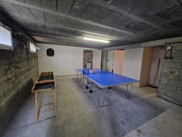 A room with a ping pong table, a dartboard, and a wooden rack.