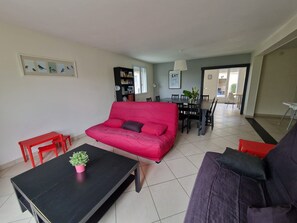 A living room with a red sofa, a black coffee table, and a purple sofa. There is a dining table with chairs in the background.