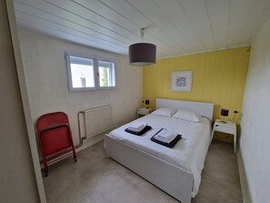 A bedroom with a bed, a red chair, a window, a radiator, and a wall with a framed picture.