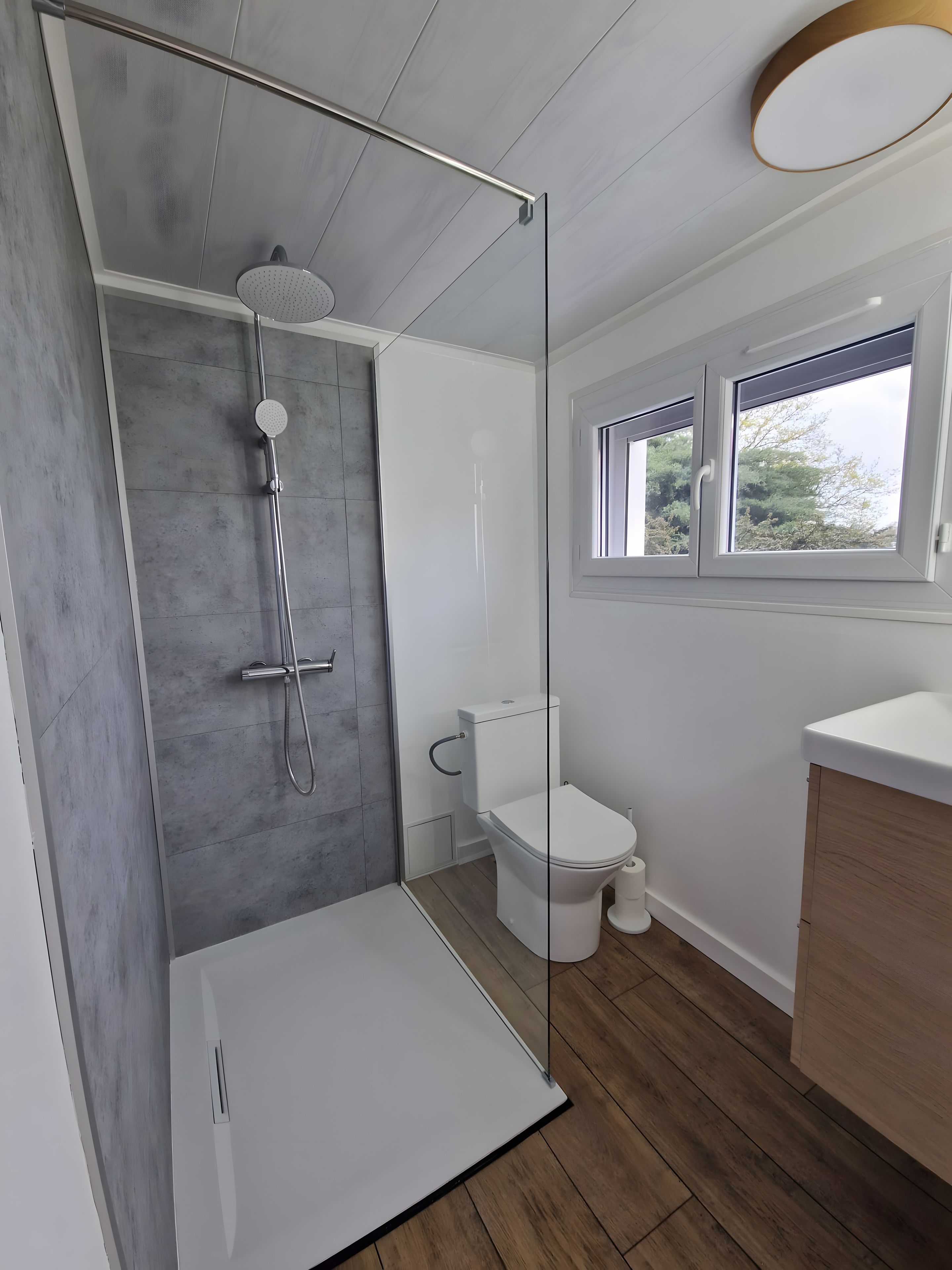 Et moderne badeværelse med brusekabine i glas, toilet og et vindue.