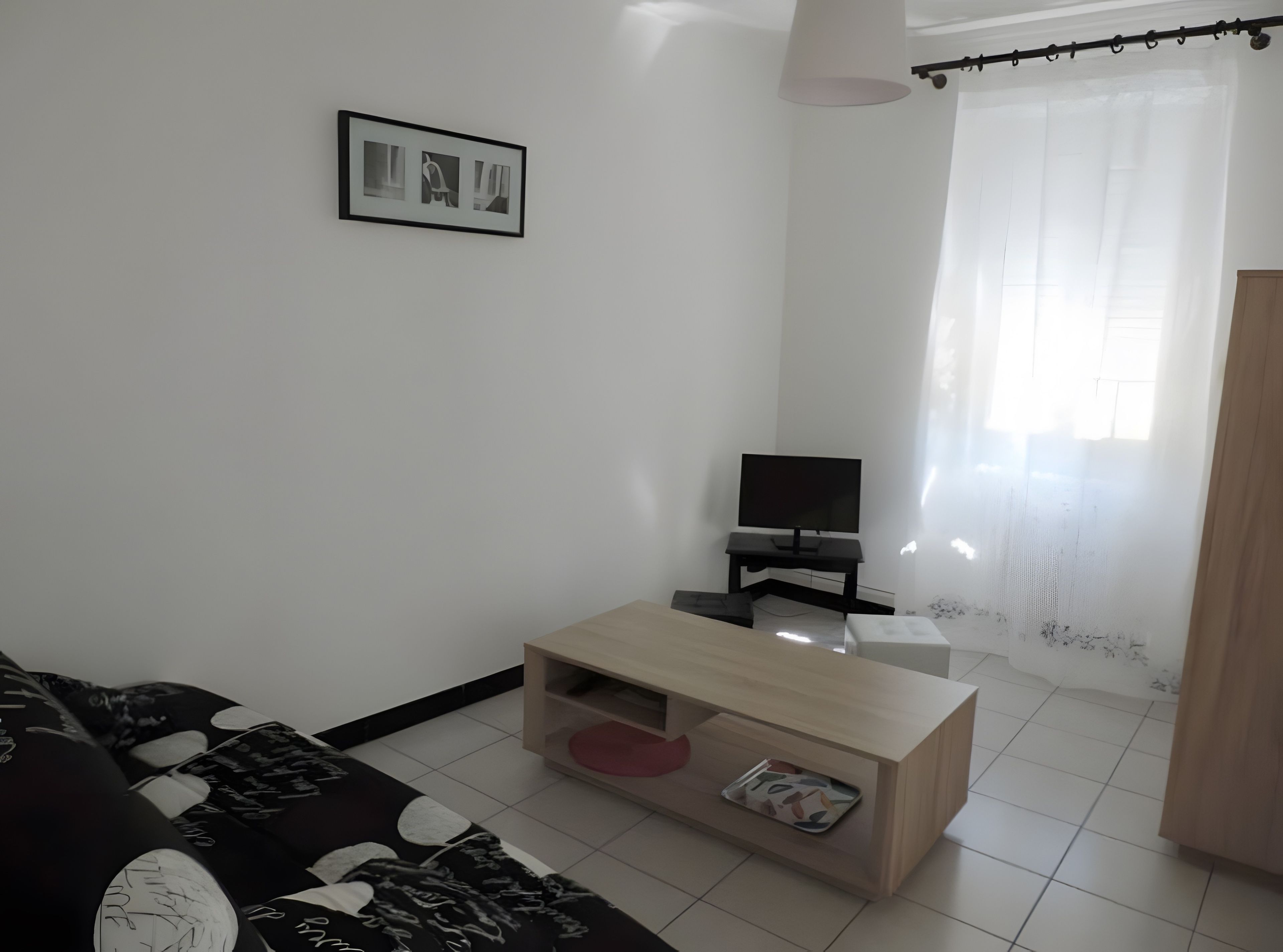 Ein Wohnzimmer mit einer Couch, einem Couchtisch, einem Fernseher und einem Fenster mit Vorhängen.