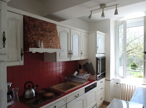 A kitchen with white cabinets, a red backsplash, a gas stove, and a window with a view of greenery.