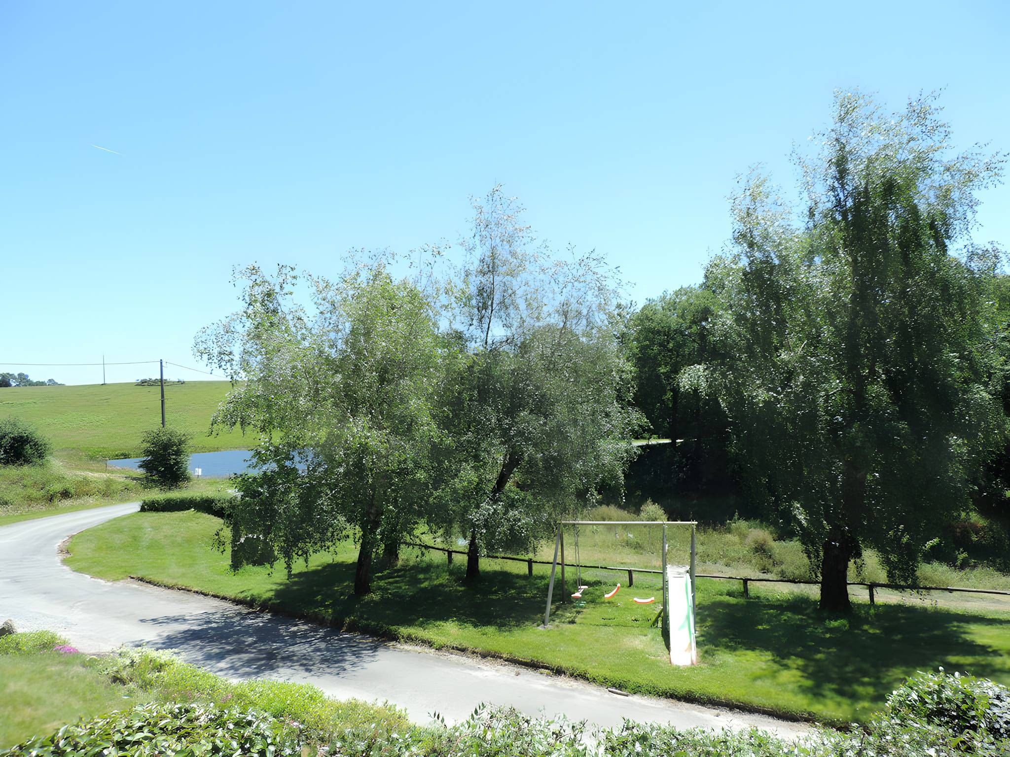 A rural road curving through a green landscape with trees and a clear sky.