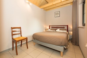 A bedroom with a wooden bed, a chair, a nightstand, and a framed picture on the wall. - Holiday Home 'Maisonnette De Sotteville Sur Mer' with Private Terrace, Private Garden and Wi-Fi (Sotteville-sur-Mer)