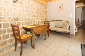 A stone wall, a wooden table with chairs, and a vintage sofa in a room with tiled flooring. - Holiday Home 'Maisonnette De Sotteville Sur Mer' with Private Terrace, Private Garden and Wi-Fi (Sotteville-sur-Mer)