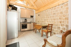 A compact kitchen with a stone wall, wooden cabinets, a microwave, a coffee maker, and a dining area with a table and chairs. - Holiday Home 'Maisonnette De Sotteville Sur Mer' with Private Terrace, Private Garden and Wi-Fi (Sotteville-sur-Mer)