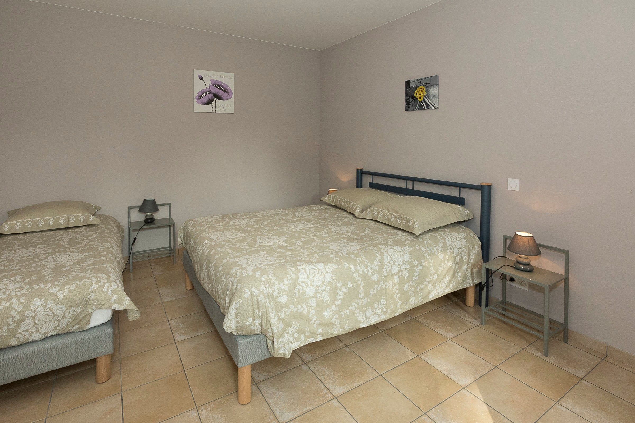 A bedroom with two single beds, a larger bed, a nightstand with a lamp, and a wall-mounted picture.
