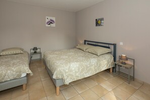 Ein Schlafzimmer mit zwei Einzelbetten, einem Doppelbett, einem Nachttisch mit Lampe und einem an der Wand hängenden Bild.