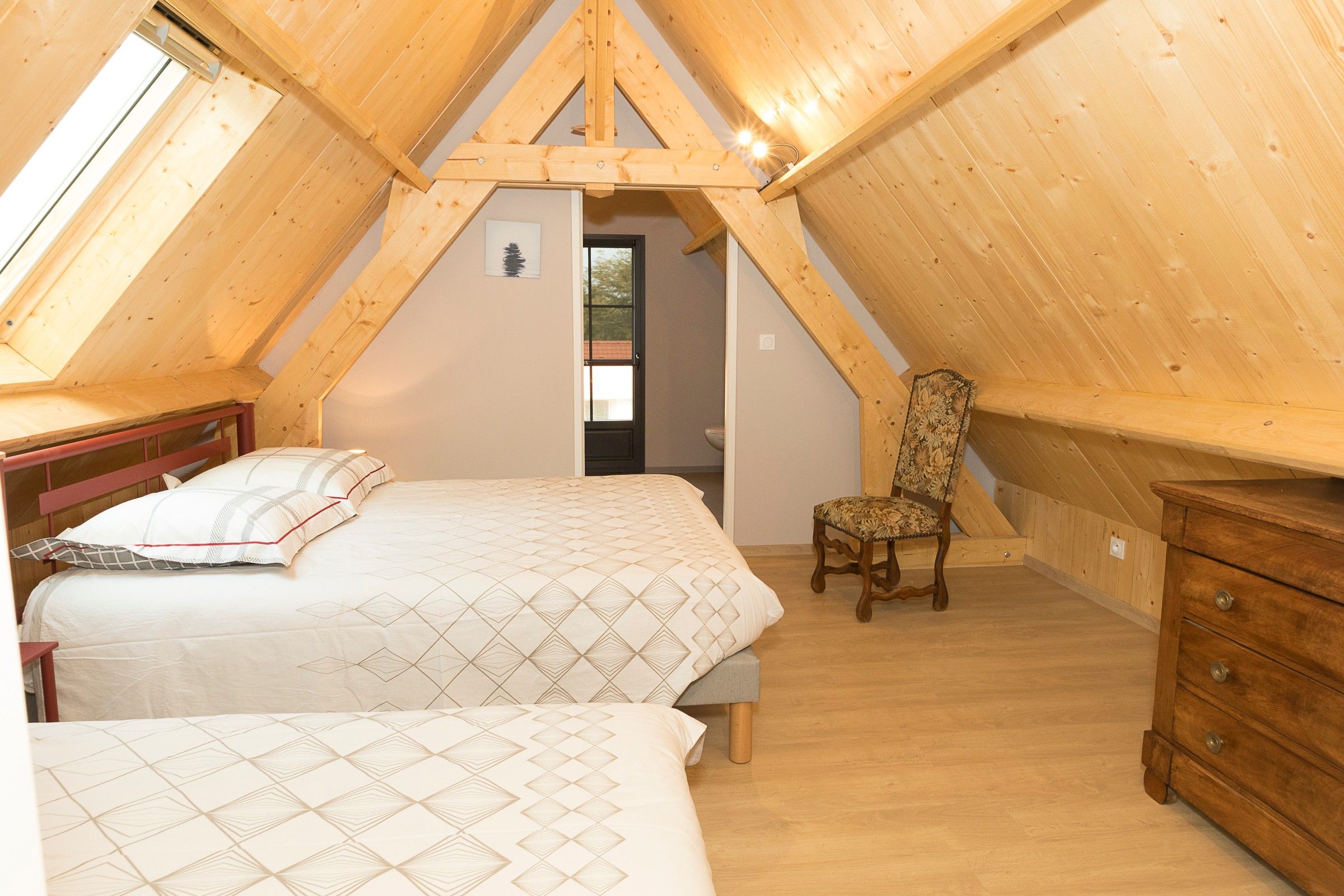 A bedroom with two beds, a chair, a dresser, and a door leading to another room.
