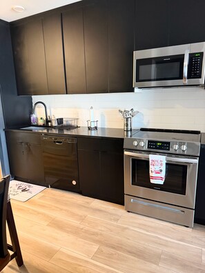 Ett modernt kök med svarta skåp, en mikrovågsugn i rostfritt stål, en diskmaskin och en ugn.