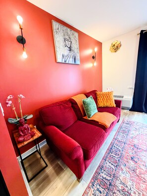 A red sofa with cushions, a small table with a Buddha statue, a wall with a Buddha painting, and a patterned rug. - Peaceful 2-bedroom, 2-bathroom Luxury with AC, Elevator in vibrant Philadelphia (Philadelphia)