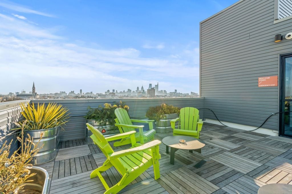 A rooftop terrace with green chairs, a small table, and potted plants.