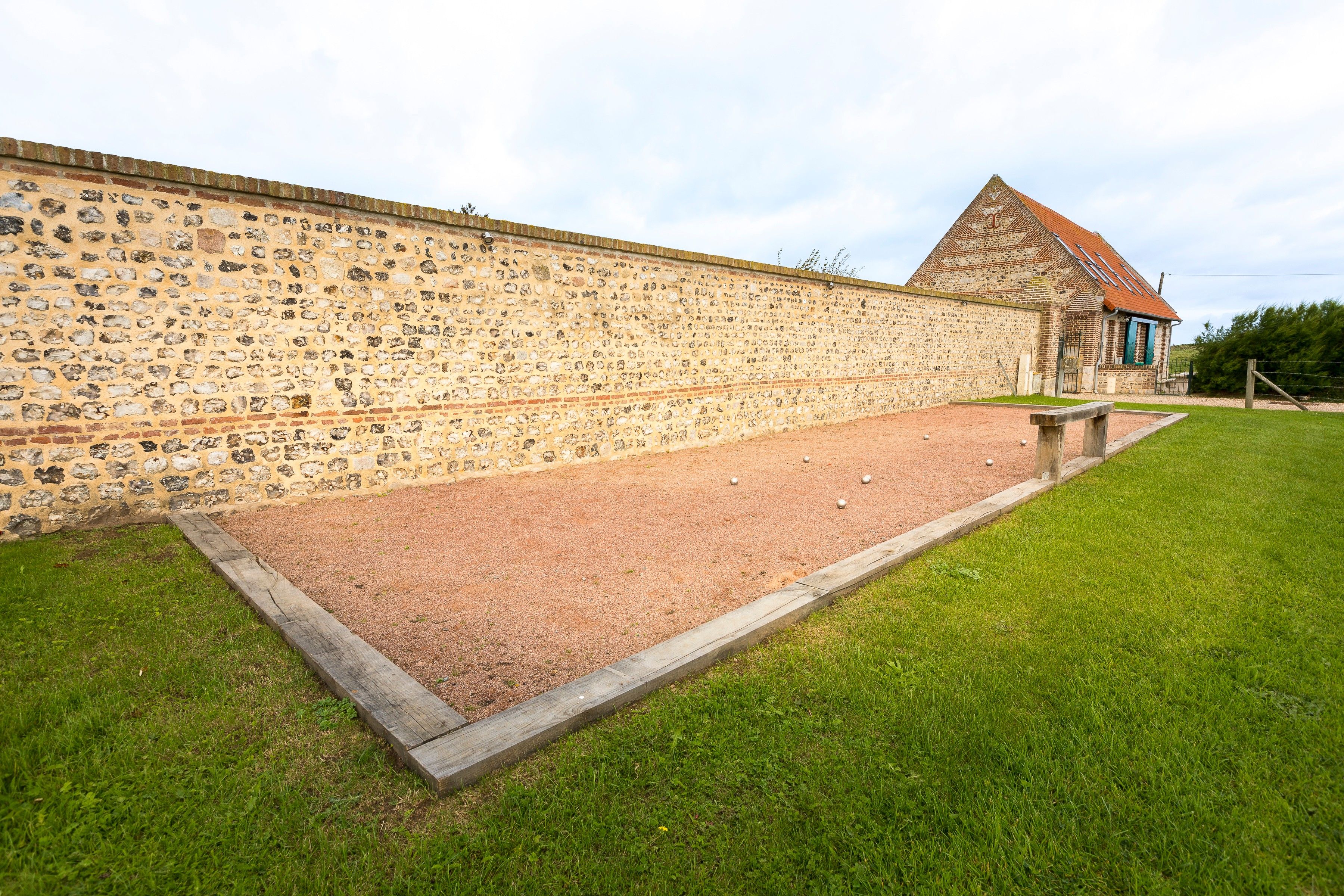 Ein Innenhof mit Steinmauer, Kiesfläche und einem Gebäude mit rotem Dach.