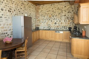 Eine Küche mit Steinwänden, Holzschränken, einem Kühlschrank, einer Spüle und einem Esstisch mit Stühlen.