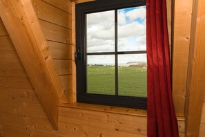 A room with a wooden sloped ceiling and a window with a black frame and red curtains. - Cottage 'Le Four À Pain' with Private Terrace and Wi-Fi (Saint-Aubin-sur-Mer)