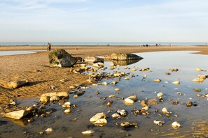 Een strand met verspreide rotsen en kalm water, een heldere lucht en mensen in de verte.