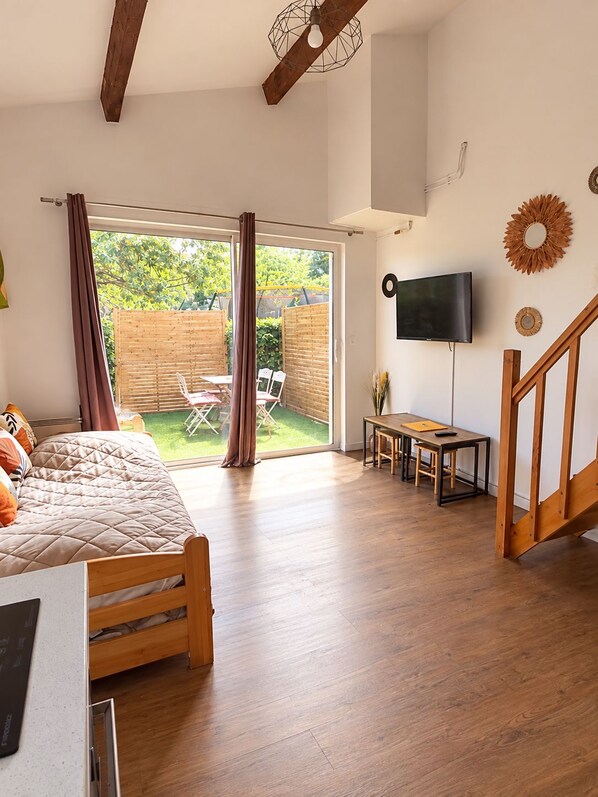 A bedroom with a bed, a desk, a TV, and a view of the outdoors.