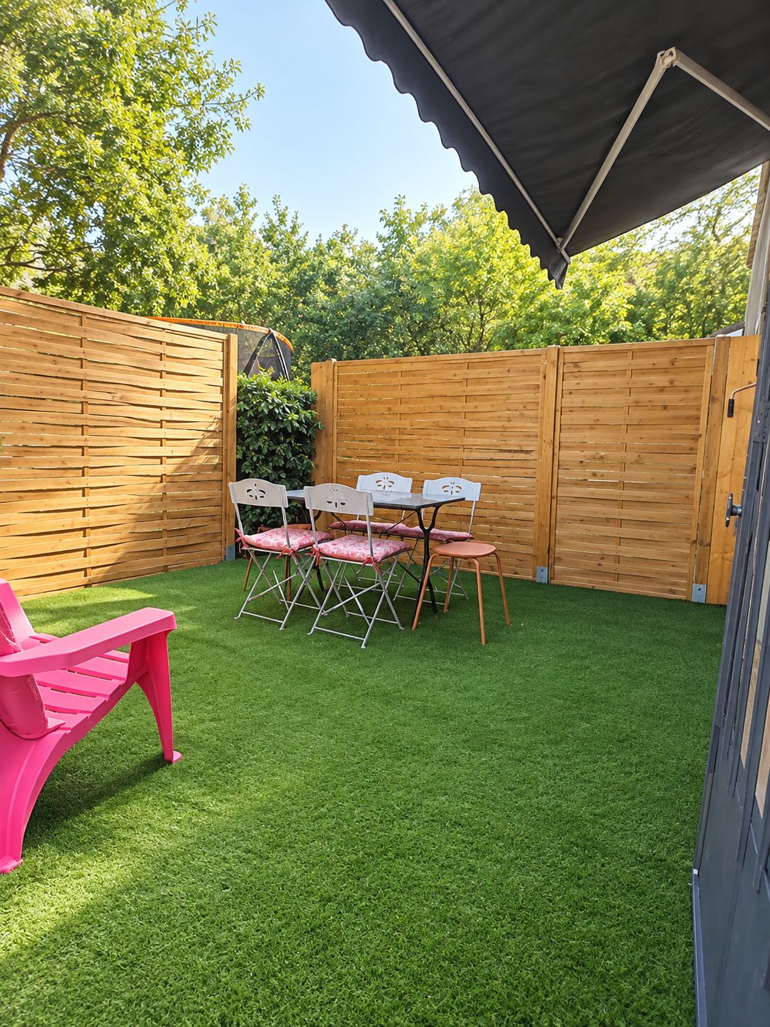 A backyard with a patio area, a table with chairs, and a pink chair.