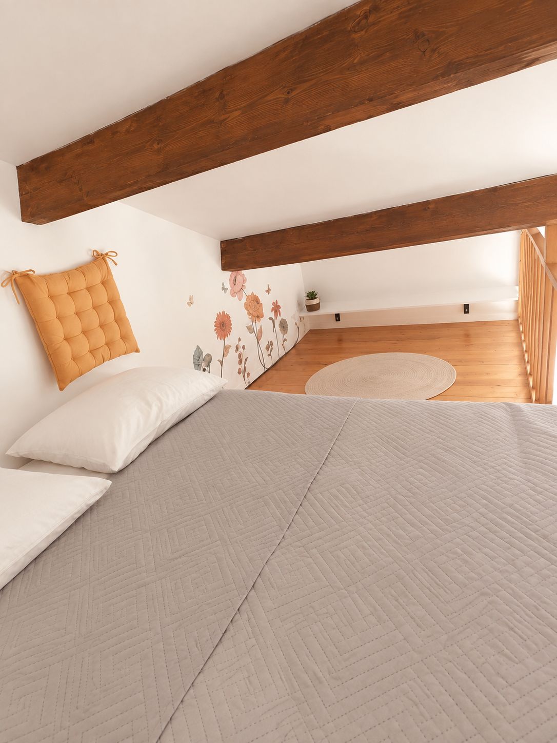 A bedroom with a loft-style ceiling, a bed with a quilted bedspread, a cushion, and a wall with floral decals.