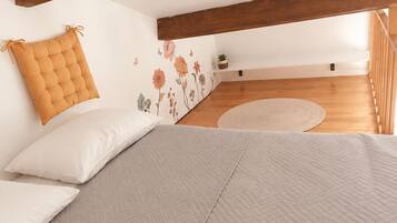 A bedroom with a loft-style ceiling, a bed with a quilted bedspread, a cushion, and a wall with floral decals.