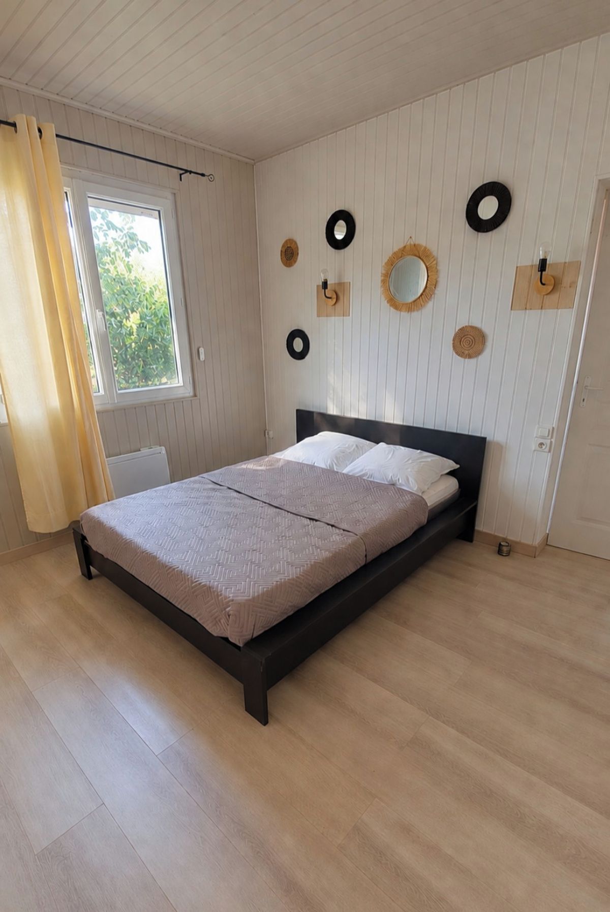 Une chambre à coucher avec un lit, une fenêtre avec des rideaux et des éléments de décoration fixés au mur.