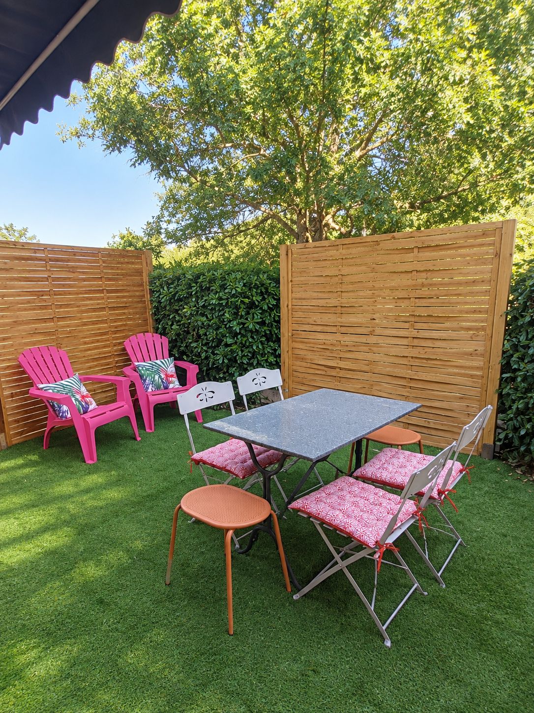 Een terras buiten met een tafel en stoelen, omgeven door een houten hek en begroeiing.