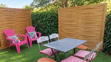 Een terras buiten met een tafel en stoelen, omgeven door een houten hek en begroeiing.
