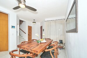 Ein Essbereich mit einem Holztisch, Stühlen, einem Deckenventilator und einer Treppe, die in einen anderen Raum führt.