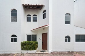 A building with multiple windows, a central door, and a small garden area. - Quiet 3BR townhouse in gated Playacar (Playa del Carmen)
