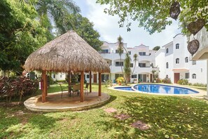 A thatched gazebo, a swimming pool, and a building with multiple balconies. - Quiet 3BR townhouse in gated Playacar (Playa del Carmen)
