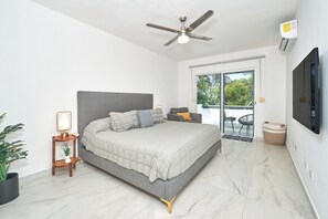 Ein modernes Schlafzimmer mit einem Bett, einem Deckenventilator, einem Fernseher und Blick ins Freie.