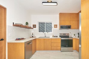 A modern kitchen with wooden cabinets, a stainless steel oven, a microwave, and a dishwasher. - Quiet 3BR townhouse in gated Playacar (Playa del Carmen)