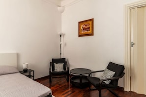 A bedroom with a bed, two chairs, a small table, a lamp, and a door. - A roomy and comfy 100 sqm apartment, ideal for four people, on the second floor of a building (with elevator; though NOT suitable for people with disabilities due to several steps at the entrance). It is situated in the elegant and quiet Della Vittoria d (Rome)