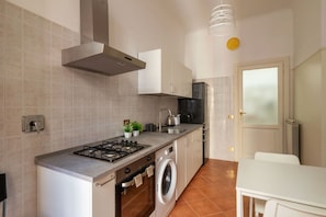 A compact kitchen with a gas stove, oven, and washing machine, a small sink, and a white table. - A roomy and comfy 100 sqm apartment, ideal for four people, on the second floor of a building (with elevator; though NOT suitable for people with disabilities due to several steps at the entrance). It is situated in the elegant and quiet Della Vittoria d (Rome)