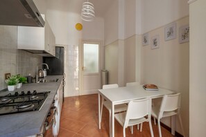 A modern kitchen with a gas stove, white cabinets, and a dining area with a white table and chairs. - A roomy and comfy 100 sqm apartment, ideal for four people, on the second floor of a building (with elevator; though NOT suitable for people with disabilities due to several steps at the entrance). It is situated in the elegant and quiet Della Vittoria d (Rome)