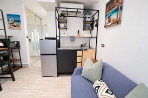 A compact living space with a kitchenette, a sofa with patterned cushions, and a door leading to another room. - Solara Pine & Tide — Beach Studio in Isla Verde <br>Welcome to Solara Pine & Tide, a cozy and efficient 215 sq ft beach apartment located in Condominium Dalia 15 on Dalia Street — right in the heart of Isla Verde. (Carolina)
