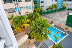 A rooftop swimming pool with palm trees, a green fence, and a view of buildings. - Solara Pine & Tide — Beach Studio in Isla Verde <br>Welcome to Solara Pine & Tide, a cozy and efficient 215 sq ft beach apartment located in Condominium Dalia 15 on Dalia Street — right in the heart of Isla Verde. (Carolina)