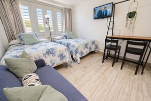 A bedroom with two beds, a desk, and a chair. - Solara Pine & Tide — Beach Studio in Isla Verde <br>Welcome to Solara Pine & Tide, a cozy and efficient 215 sq ft beach apartment located in Condominium Dalia 15 on Dalia Street — right in the heart of Isla Verde. (Carolina)