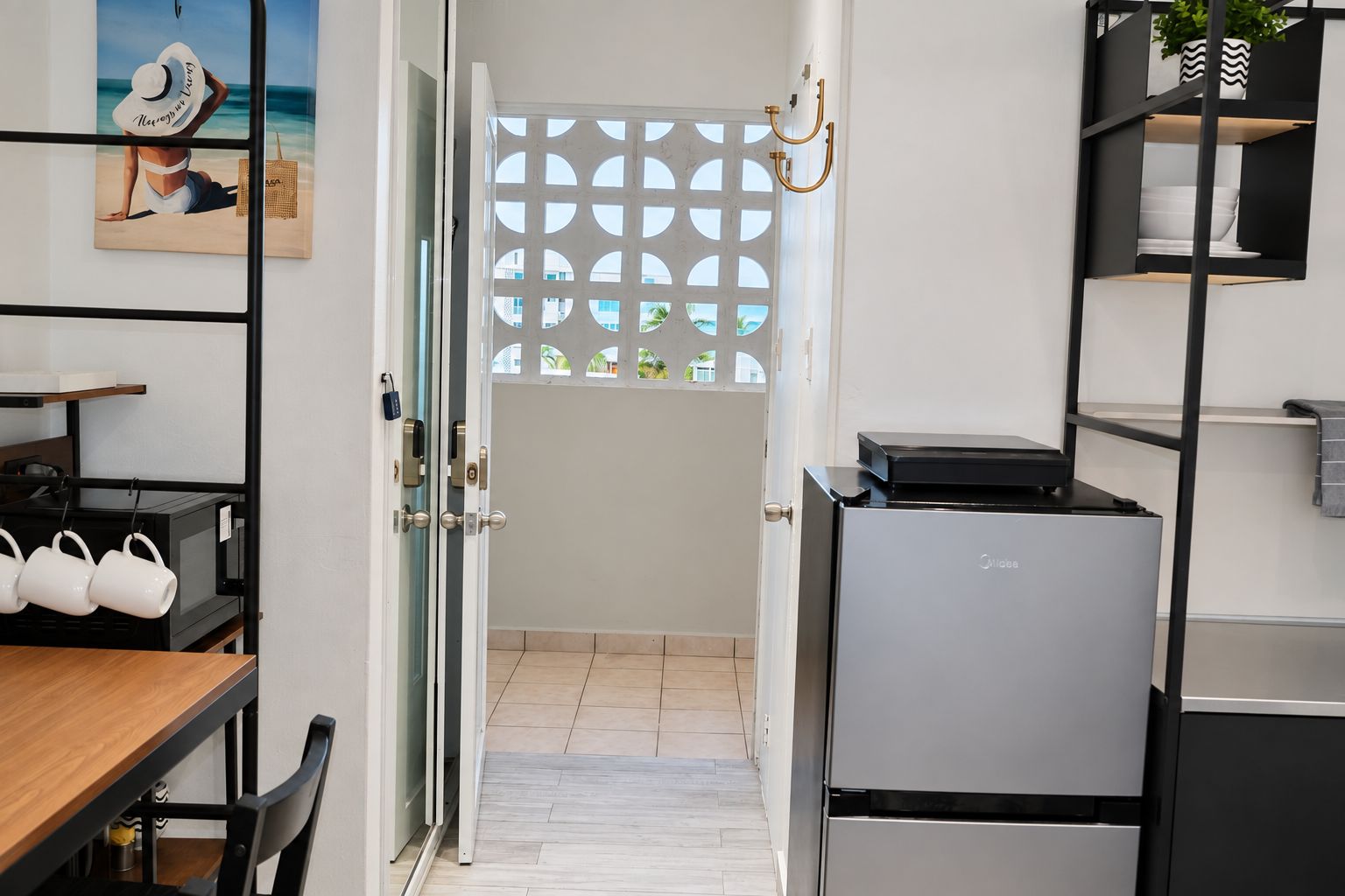 A kitchen with a refrigerator, a dining table with chairs, and a view through a door with a decorative screen.