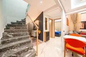 Een modern interieur met een marmeren trap, een eethoek met oranje stoelen en een slaapkamer met een blauw bed.
