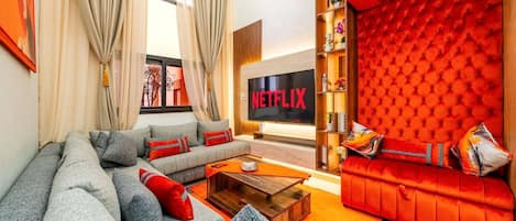 A modern living room with a grey sofa, red upholstered sofa, and a Netflix TV.