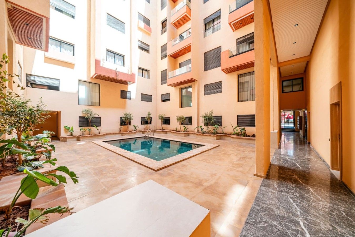 Un bâtiment moderne doté d’une piscine centrale, de nombreux balcons et d’un sol carrelé et impeccable.
