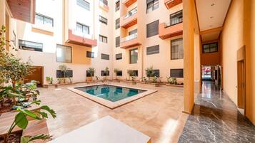 Un bâtiment moderne doté d’une piscine centrale, de nombreux balcons et d’un sol carrelé et impeccable.