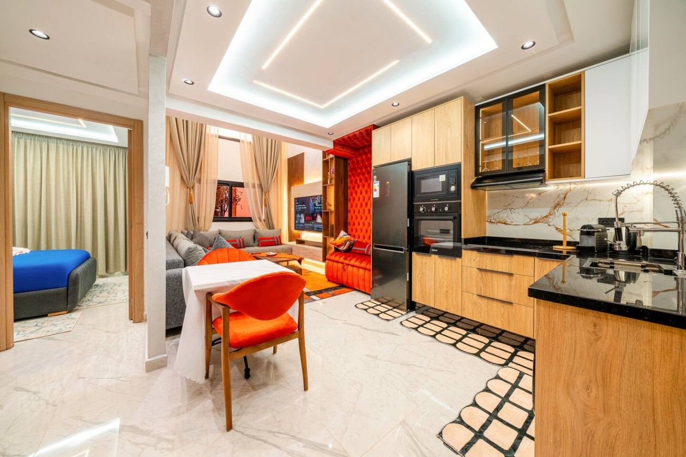 Une chambre d’hôtel moderne dotée d’un coin repas, d’une kitchenette et d’un canapé, avec un mur d’accent de couleur rouge.