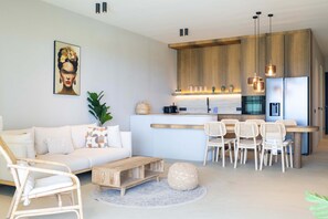 A modern kitchen with wooden cabinets, a dining area with wicker chairs, and a white sofa. - Solara - Luxury 3-bedroom Home With Private Pool (Sint Michiel)