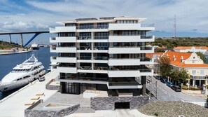 A multi-story building with balconies, a marina with boats, and a bridge in the background. - NEW Harbour Nine at The Wharf Urban Elegance (Willemstad)