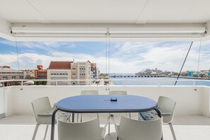 A balcony with a round table and chairs, overlooking a marina with boats and buildings. - NEW Harbour Nine at The Wharf Urban Elegance (Willemstad)